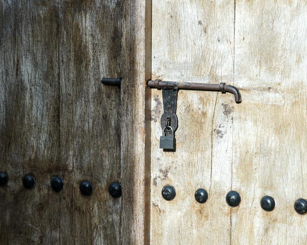Close-up of a weathered wooden door with a vintage iron padlock in sunlight.